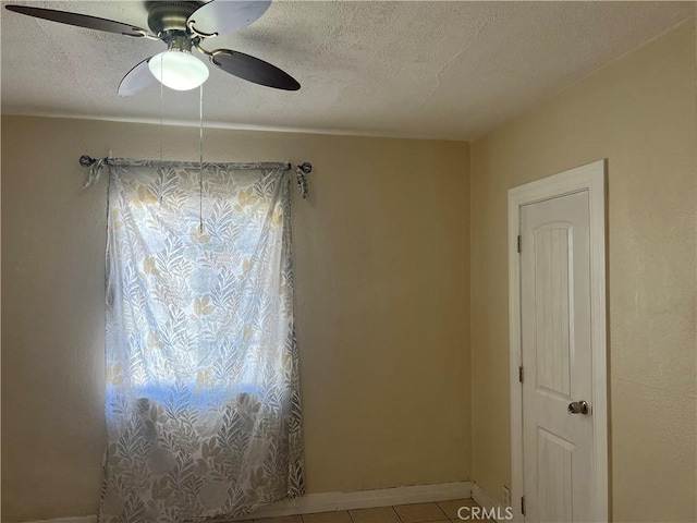 tiled empty room with baseboards, a textured ceiling, and ceiling fan