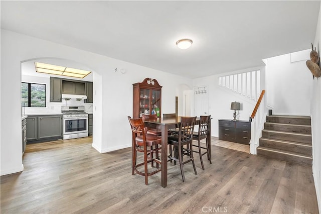 dining room featuring stairway, baseboards, arched walkways, and light wood-type flooring