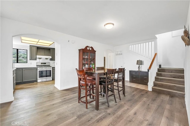 dining space with arched walkways, stairway, light wood finished floors, and baseboards