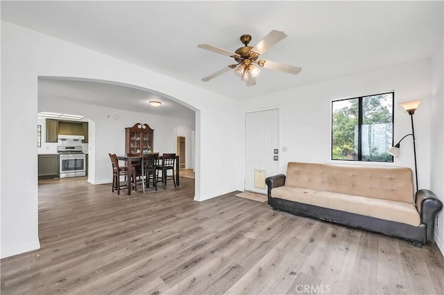 living area featuring arched walkways, baseboards, ceiling fan, and wood finished floors