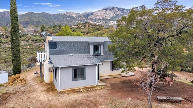 rear view of house with a mountain view, roof with shingles, and stucco siding