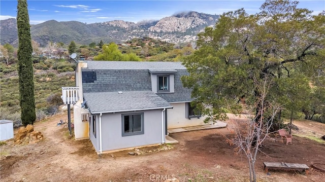 view of home's exterior featuring a chimney, a mountain view, a shingled roof, and stucco siding