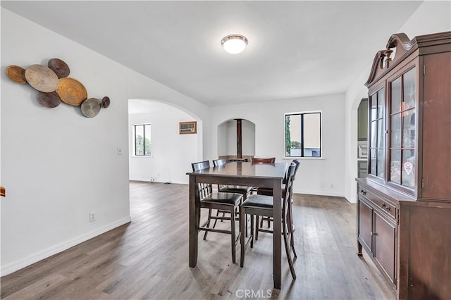 dining room with arched walkways, dark wood-style floors, and baseboards