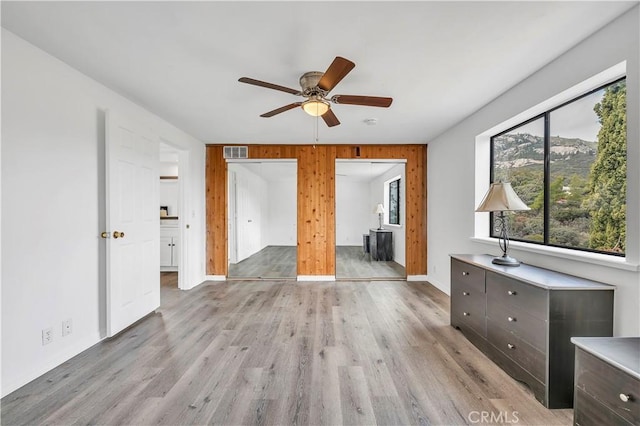 unfurnished bedroom with visible vents, baseboards, ceiling fan, wood walls, and light wood-type flooring