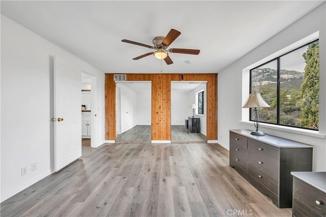 unfurnished bedroom featuring ensuite bathroom, wooden walls, light wood finished floors, baseboards, and visible vents