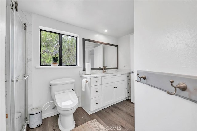 bathroom with vanity, toilet, wood finished floors, and a shower with shower door