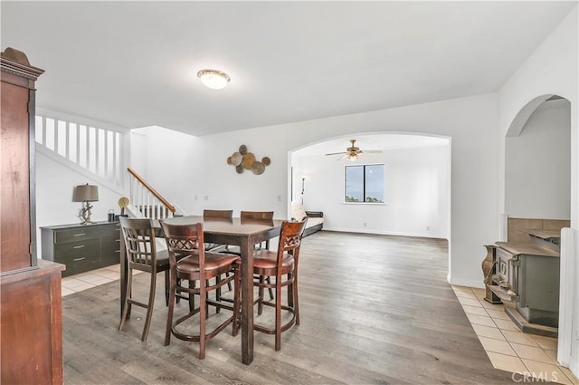 dining room with stairway, light wood-type flooring, a wood stove, arched walkways, and a ceiling fan