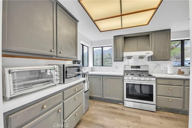 kitchen with gas range, gray cabinetry, light wood-style flooring, and range hood