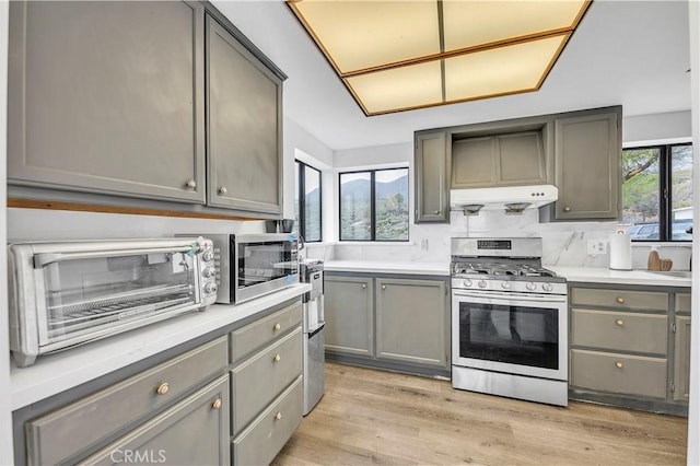 kitchen with under cabinet range hood, gray cabinetry, a toaster, and stainless steel gas range