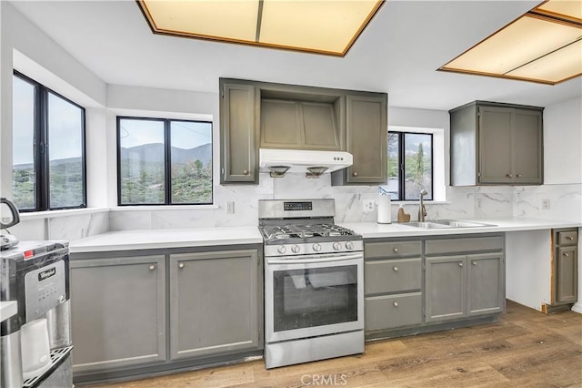 kitchen featuring gray cabinetry, gas stove, a sink, and ventilation hood