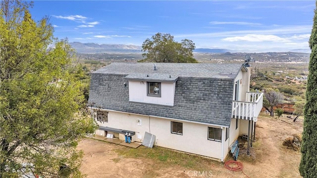 rear view of property featuring a mountain view, a gambrel roof, stucco siding, and a shingled roof