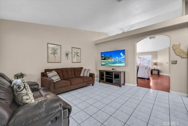 living room with visible vents, lofted ceiling, arched walkways, light tile patterned flooring, and baseboards