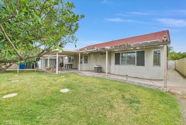 rear view of property with fence, a tiled roof, stucco siding, a lawn, and a patio area