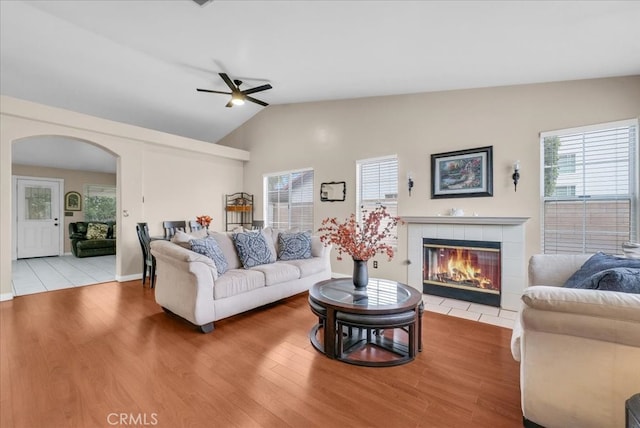 living area featuring vaulted ceiling, wood finished floors, arched walkways, and a tile fireplace