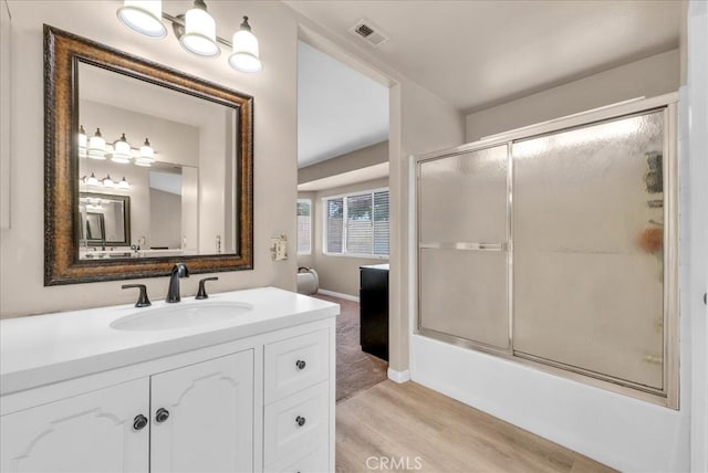 bathroom with vanity, wood finished floors, visible vents, baseboards, and combined bath / shower with glass door