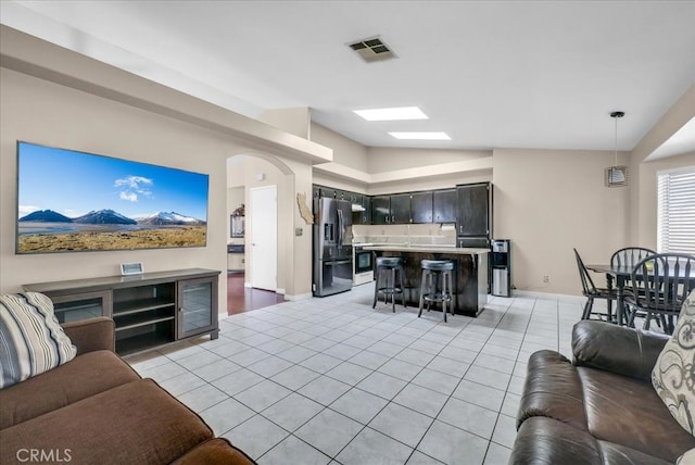 living room featuring light tile patterned floors, visible vents, vaulted ceiling with skylight, and baseboards