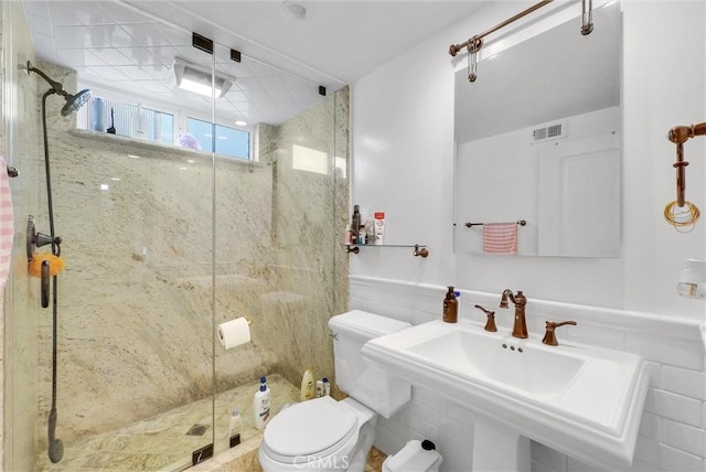 bathroom featuring visible vents, toilet, a sink, wainscoting, and a shower stall