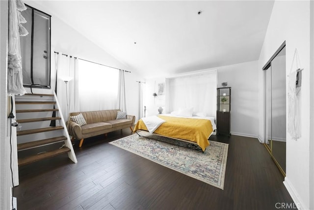 bedroom with vaulted ceiling, wood finished floors, baseboards, and a closet