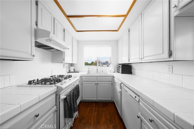 kitchen featuring white appliances, tile countertops, dark wood finished floors, a sink, and under cabinet range hood