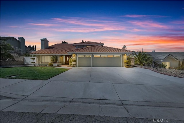 mediterranean / spanish home featuring concrete driveway, a tile roof, stucco siding, a garage, and a yard