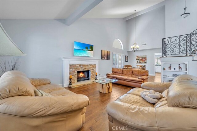 living room featuring visible vents, vaulted ceiling with beams, hardwood / wood-style floors, a stone fireplace, and an inviting chandelier