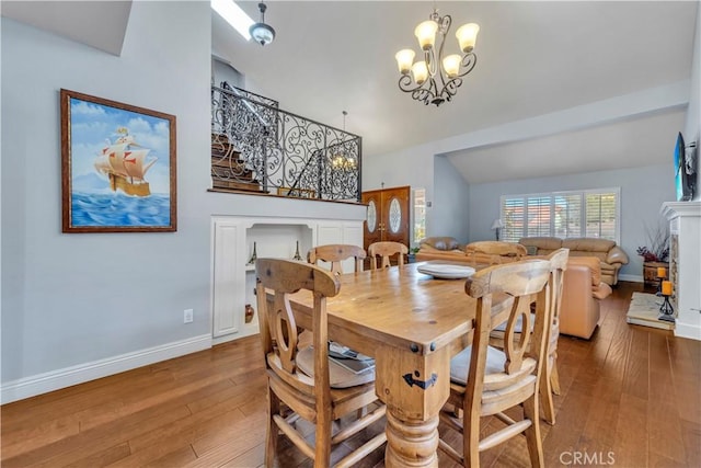 dining space featuring vaulted ceiling, a notable chandelier, baseboards, and hardwood / wood-style flooring