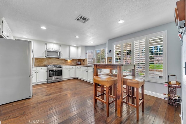 kitchen featuring dark wood-style floors, decorative backsplash, stainless steel appliances, and visible vents