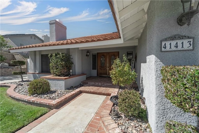 view of exterior entry with a tile roof and stucco siding