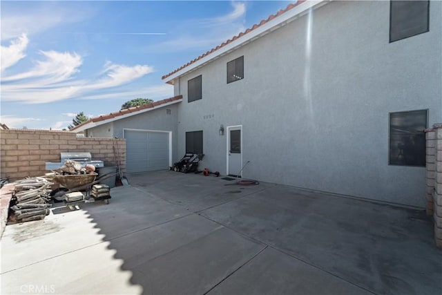 rear view of house featuring fence, stucco siding, a garage, driveway, and a patio