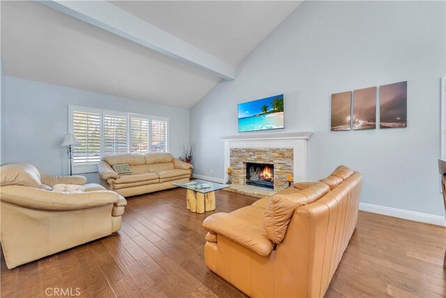 living room with a stone fireplace, beamed ceiling, baseboards, and wood finished floors