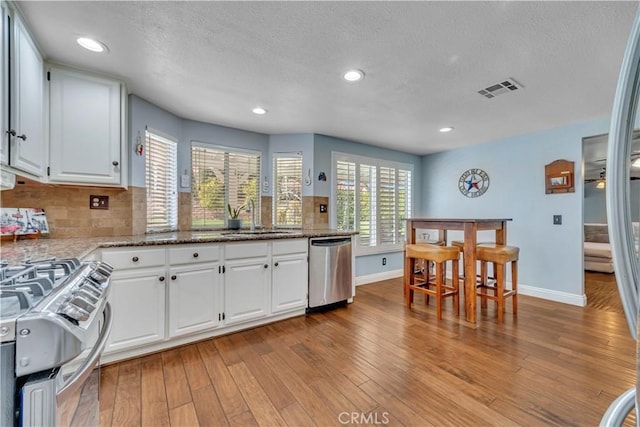 kitchen featuring visible vents, a sink, stainless steel appliances, light wood-style floors, and white cabinets