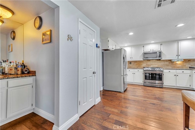 kitchen featuring stainless steel appliances, wood-type flooring, visible vents, and decorative backsplash