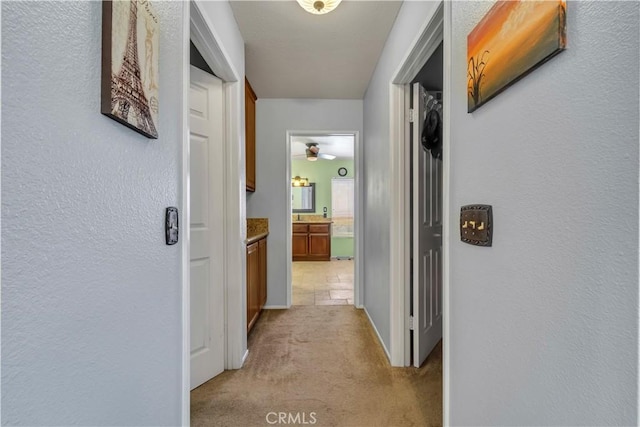 corridor featuring light colored carpet and a textured wall