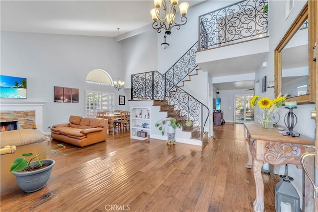 entrance foyer with wood finished floors, stairs, a stone fireplace, a towering ceiling, and a chandelier