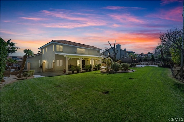 back of house at dusk featuring stucco siding, a patio, a lawn, and fence