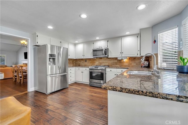 kitchen with dark stone countertops, appliances with stainless steel finishes, dark wood-style floors, white cabinetry, and a sink