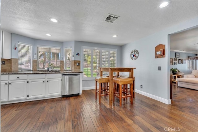 kitchen featuring visible vents, a sink, dishwasher, decorative backsplash, and dark wood-style flooring