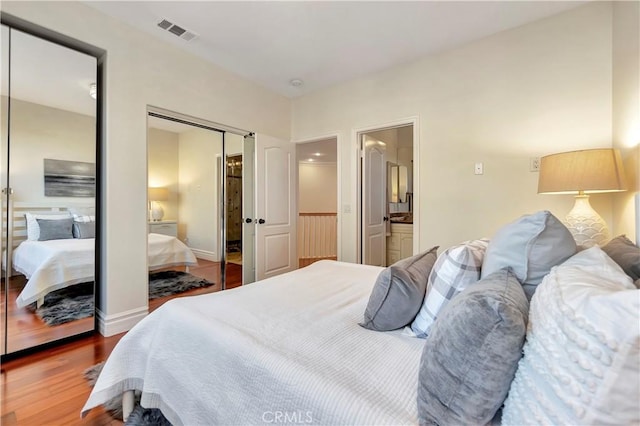 bedroom with visible vents, two closets, baseboards, ensuite bathroom, and wood finished floors