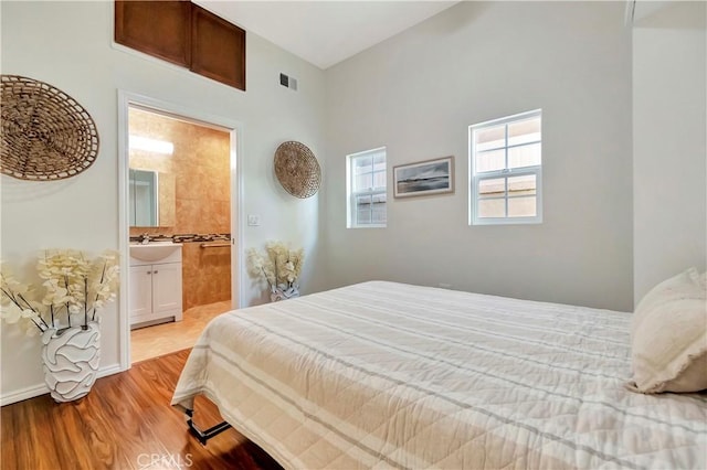 bedroom featuring baseboards, visible vents, ensuite bath, a sink, and light wood-type flooring