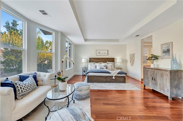 bedroom featuring a raised ceiling, wood finished floors, and visible vents