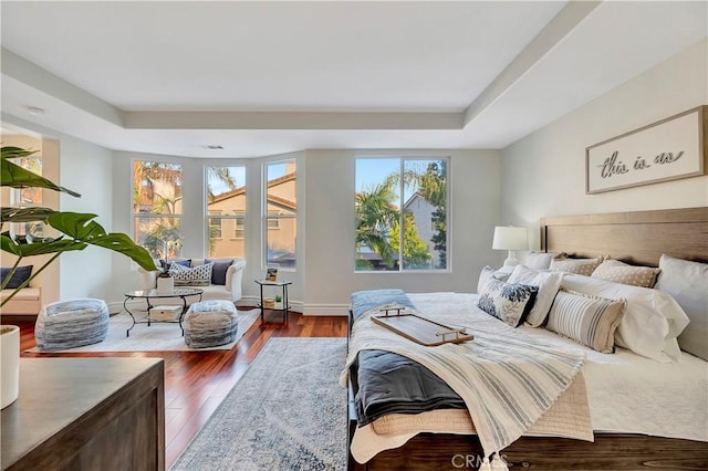 bedroom featuring visible vents, baseboards, a tray ceiling, and wood finished floors