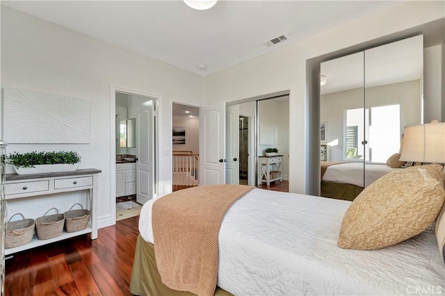 bedroom with visible vents, two closets, wood finished floors, and ensuite bathroom