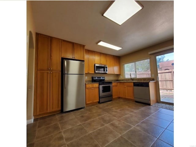 kitchen with dark tile patterned flooring, brown cabinetry, arched walkways, and stainless steel appliances