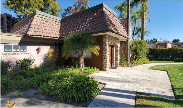 exterior space with stone siding, stucco siding, mansard roof, and a tile roof