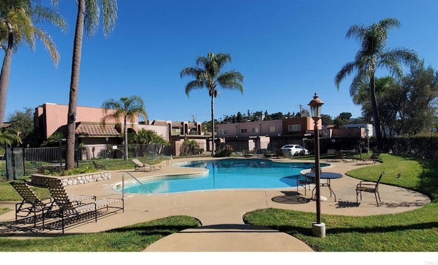 community pool with a lawn, a patio area, fence, and a residential view