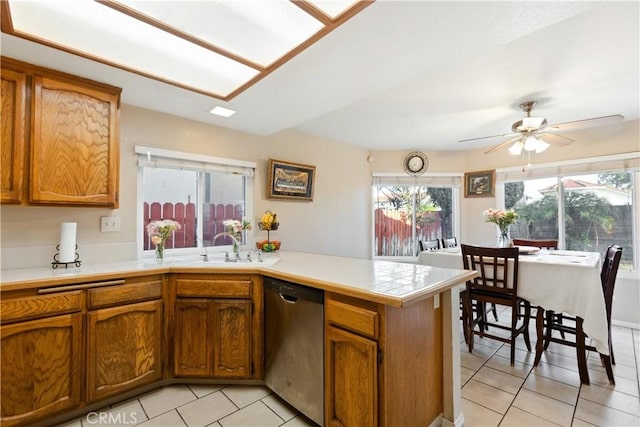 kitchen featuring a healthy amount of sunlight, a peninsula, stainless steel dishwasher, brown cabinetry, and a sink