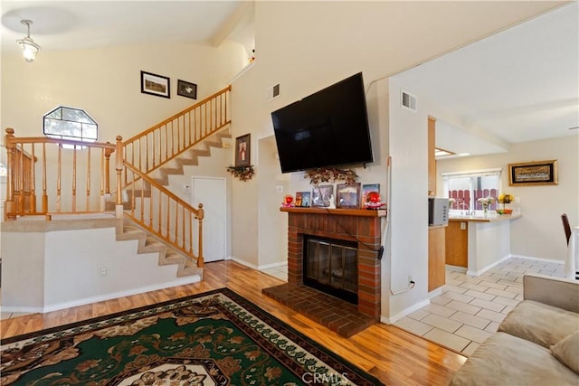 living area featuring a brick fireplace, stairway, wood finished floors, and visible vents