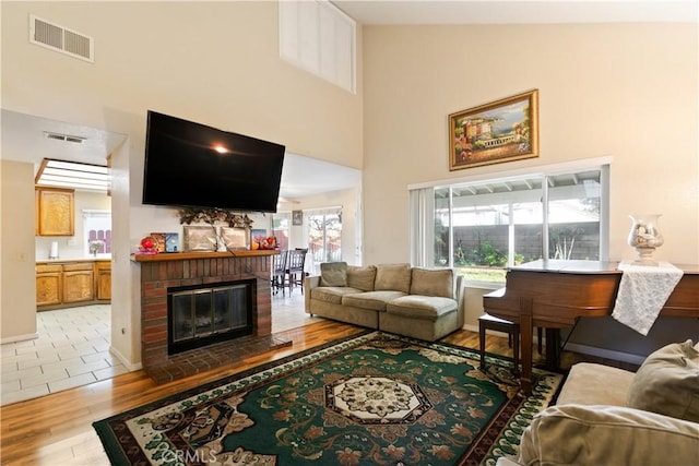 living area with visible vents, light wood-style floors, a brick fireplace, and a towering ceiling