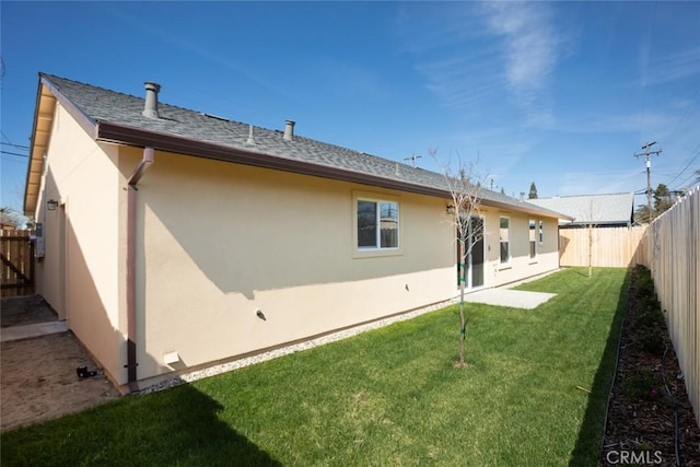 back of property with a yard, stucco siding, a fenced backyard, and roof with shingles