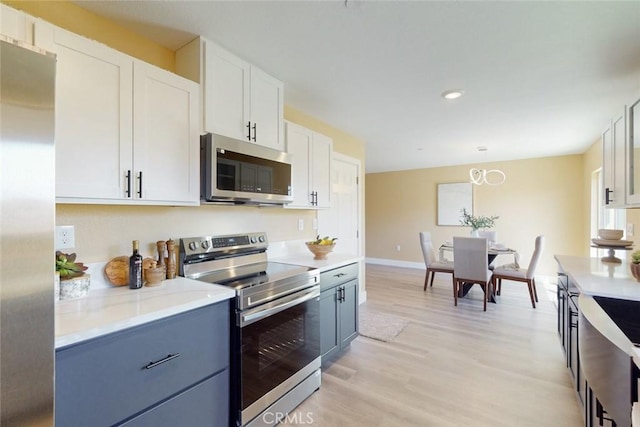 kitchen featuring light wood-type flooring, white cabinetry, stainless steel appliances, light countertops, and hanging light fixtures
